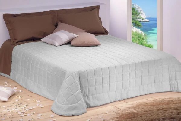 Camera da letto con trapuntina primavera estate su letto matrimoniale beige con vista mare dalla finestra